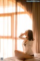 A woman sitting on a bed in front of a window.