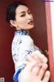 A woman in a blue and white cheongsam leaning against a red door.