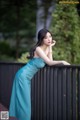 A woman in a blue dress leaning against a fence.