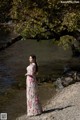 A woman in a long dress standing by a river.