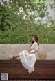 A woman sitting on a wooden bench wearing a white dress.