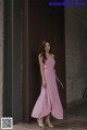 A woman in a pink dress standing in front of a wall.