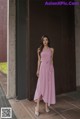 A woman in a pink dress standing in front of a wall.