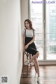 A woman sitting on a stool in front of a window.