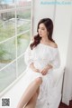 A woman in a white dress sitting on a window sill.