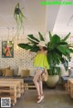 A woman standing in front of a large plant in a room.