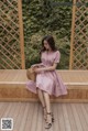 a woman sitting on a wooden bench wearing a pink dress