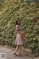 A woman standing in front of a wall covered in ivy.