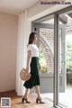 a woman standing in front of a window wearing a white t - shirt and green skirt