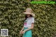 A woman wearing a straw hat standing in front of a green wall.