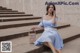 A woman in a blue and white dress sitting on some steps.