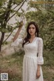 A woman in a white dress standing next to a tree.