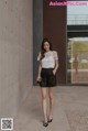 a woman standing in front of a wall wearing a white top and black shorts