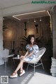 A woman sitting on a white chair in front of a brick wall.