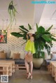 A woman standing in front of a large plant in a room.