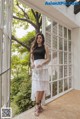 a woman standing in front of a window wearing a black top and white skirt