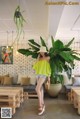 A woman standing in front of a large plant in a room.