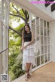 a woman standing in front of a window wearing a black top and white skirt