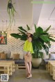 A woman standing in front of a large plant in a room.