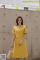 a woman wearing a yellow dress standing in front of a wall