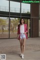 A woman wearing a pink blazer and white shorts.