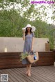 A woman in a blue dress and a white hat holding a straw bag.