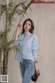 a woman standing next to a plant wearing a blue shirt and jeans