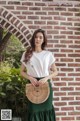 A woman standing in front of a brick wall holding a rattan bag.