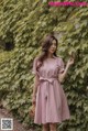 a woman standing in front of a wall wearing a pink dress