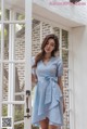 a woman standing in front of a window wearing a blue dress