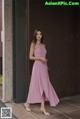 A woman in a pink dress standing in front of a wall.