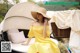 A woman in a yellow dress and straw hat sitting on a bed.