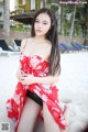 A woman in a red and white dress sitting on a beach.