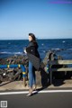 A woman standing on the side of a road next to the ocean.