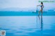 A woman in a blue bikini standing on the edge of a swimming pool.