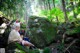 A couple of people sitting on top of a rock in the woods.