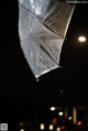 A silver umbrella hanging from a string in the rain.