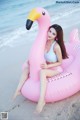 A woman sitting on an inflatable flamingo on the beach.